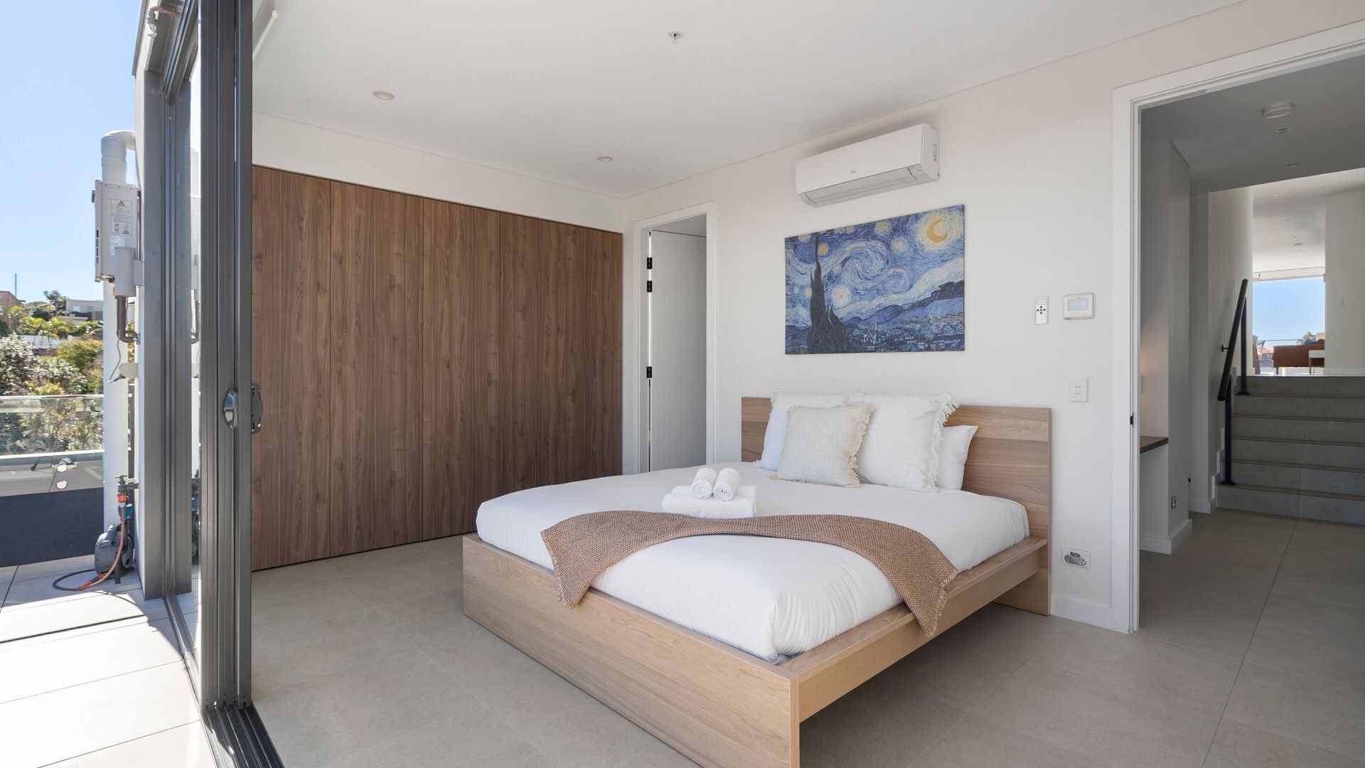 A modern bedroom with a large bed, a wooden wardrobe, and a painting on the wall.