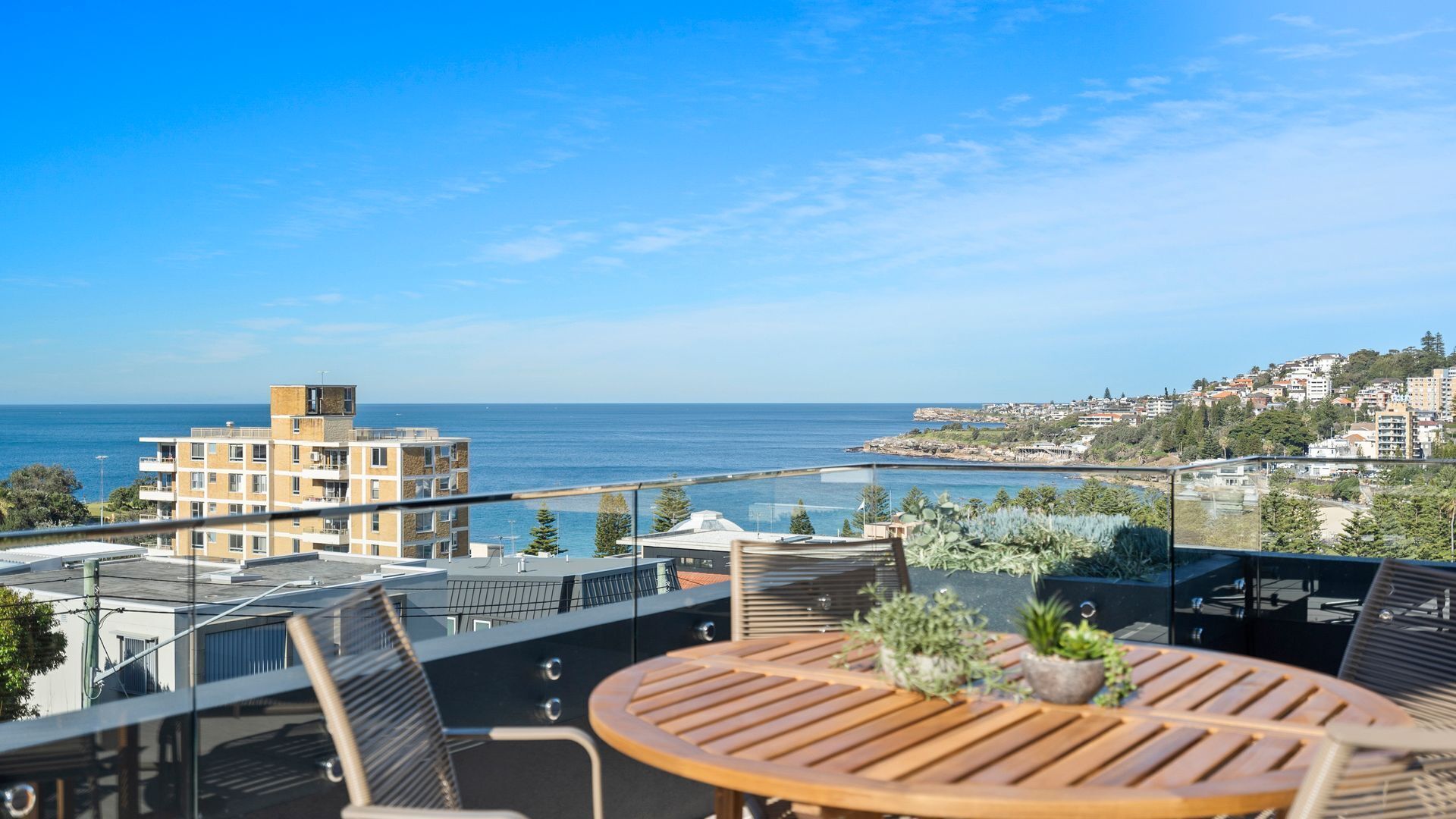 A balcony with a view of the sea, a round wooden table, and chairs.
