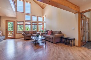 Ein geräumiges Wohnzimmer mit hoher Decke, großen Fenstern und Holzboden.