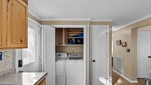Cocina compacta con lavadora y secadora integradas, armarios de madera y encimera de granito.