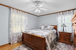 Ein Schlafzimmer mit einem hölzernen Bett, einem Nachttisch, einer Lampe, einem Deckenventilator und durchsichtigen Vorhängen.