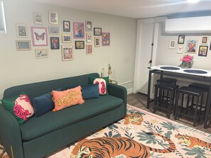 A living room with a green sofa, a tiger-themed rug, and a wall adorned with various framed artworks. - #HabitueHomes - The Tigers Nap (Boise)
