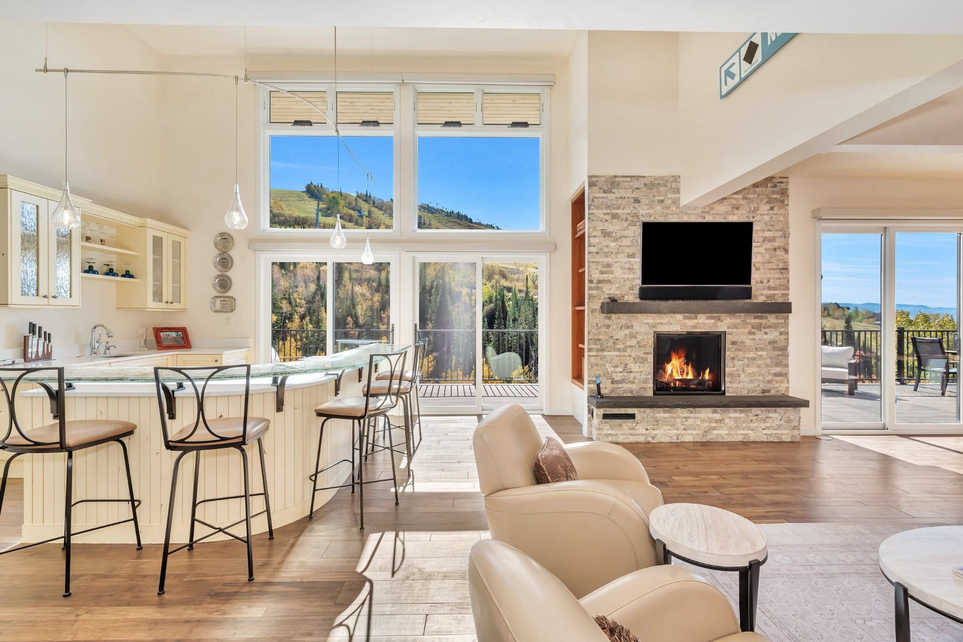 Un amplio salón con chimenea, una barra con taburetes y un ventanal con vistas al exterior.