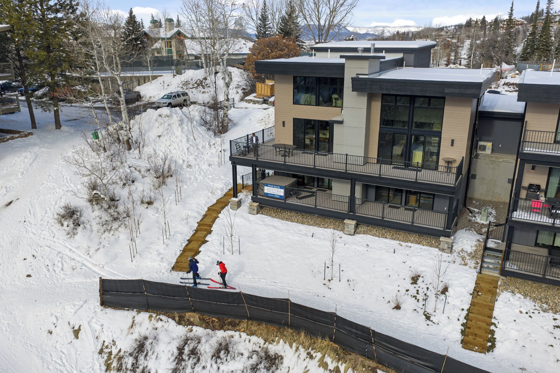 A modern building with a balcony, a ski slope, and a 'For Sale' sign.