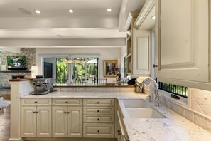 A kitchen with a large island, a built-in stove, and a sink. There is a window providing a view of the outdoors. - FPX Legacy Lodge - True Ski In Ski Out! 5-BR+Loft+Rec Room w/ Views, Private Hot Tub, Club Amenities (Steamboat Springs)