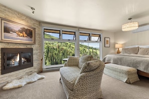 A bedroom with a fireplace, a large window with a forest view, a bed, and a sofa. - FPX Legacy Lodge - True Ski In Ski Out! 5-BR+Loft+Rec Room w/ Views, Private Hot Tub, Club Amenities (Steamboat Springs)