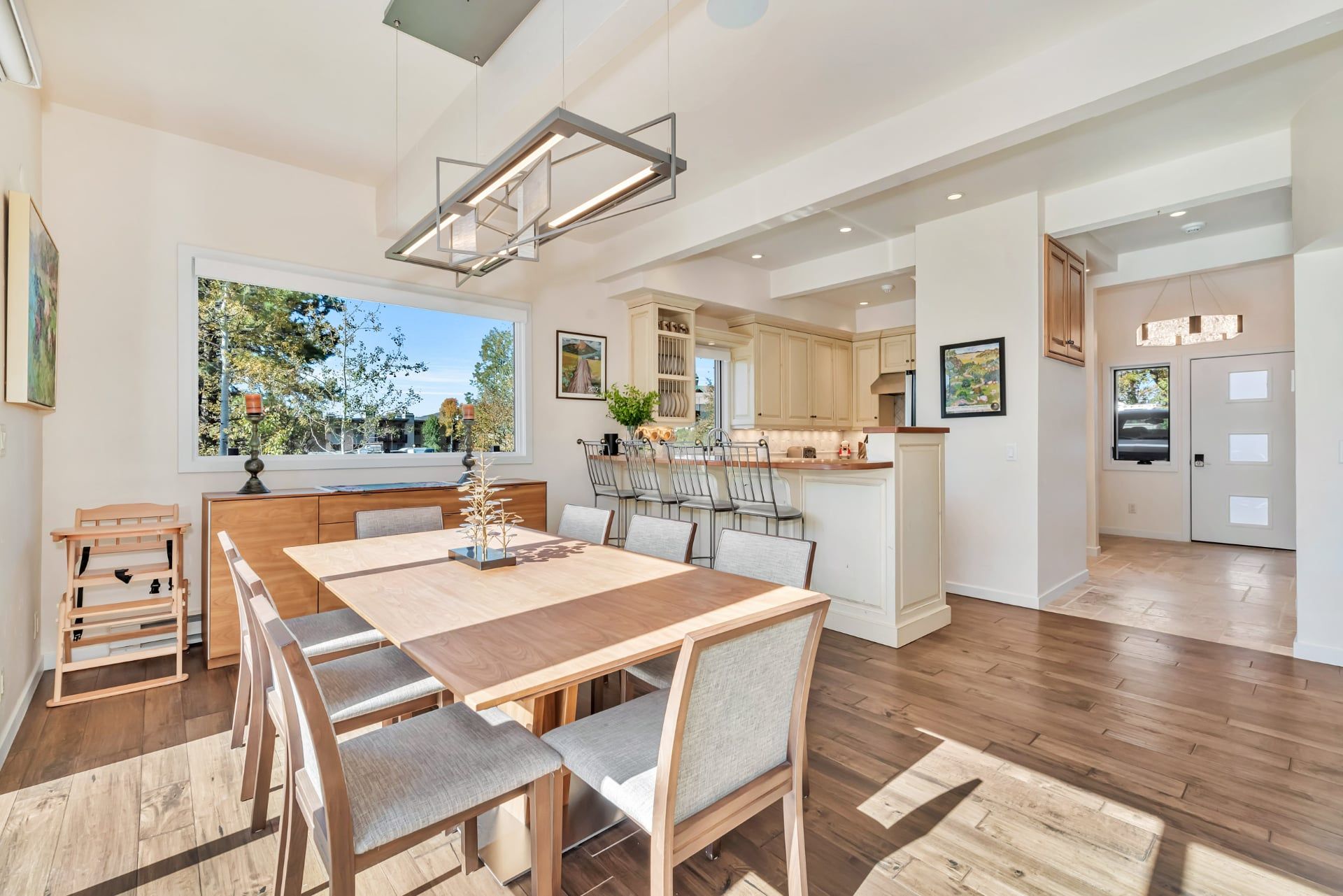 A spacious kitchen with modern appliances, a dining area with a large wooden table and chairs, and a view of the outdoors through a large window.