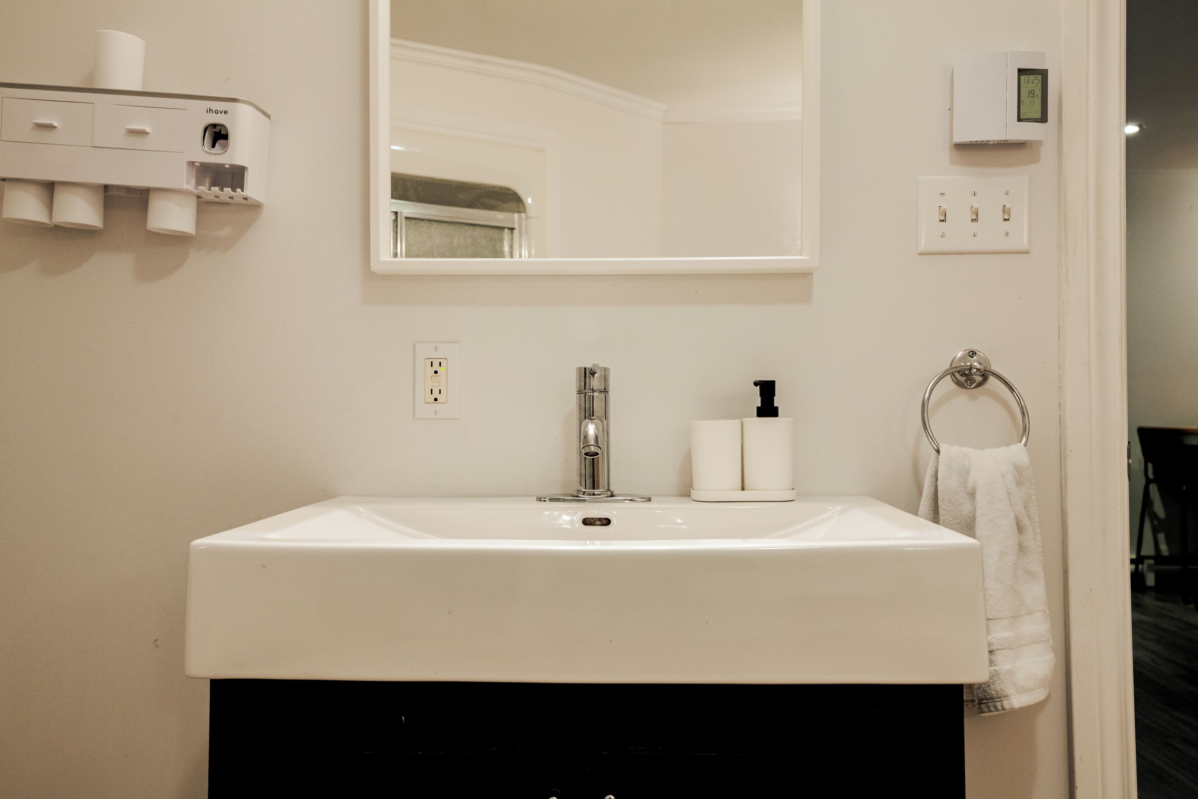 A bathroom with a white sink, a mirror, a towel ring, and a wall-mounted dispenser.