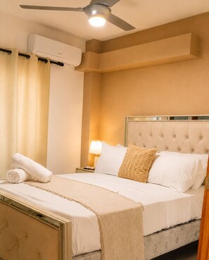 Een hotelkamer met een bed, een plafondventilator, een airconditioning, een nachtkastje, een lamp en een raam met gordijnen.