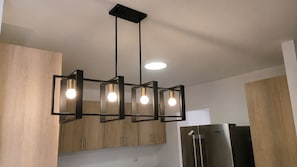 A modern kitchen with wooden cabinets, a stainless steel refrigerator, and a pendant light fixture with multiple bulbs. - Perfect 3-bedroom apartment with AC in beautiful Santiago de los Caballeros (Santiago de los Caballeros)