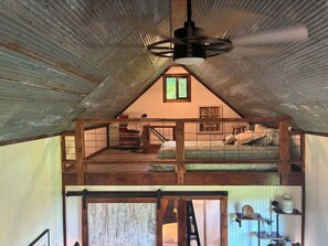 Ein Schlafzimmer im Loft-Stil mit geneigter Decke, einem Bett, einem Fenster und einem Deckenventilator.