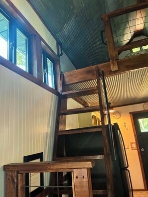 Uma escadaria de madeira em vários níveis, com corrimão de metal, conduzindo a um quarto com uma porta e um relógio na parede.