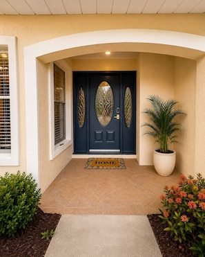 A front entrance with a dark blue door, a doormat with 'HOME' written on it, and a potted plant beside the door.