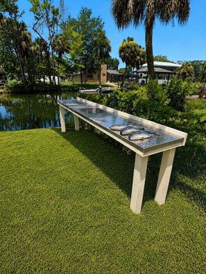 A concrete table with fish on it, located near a body of water with trees and a building in the background. - Luxury Gulf Access Retreat | Gym | Crystal River (Crystal River)