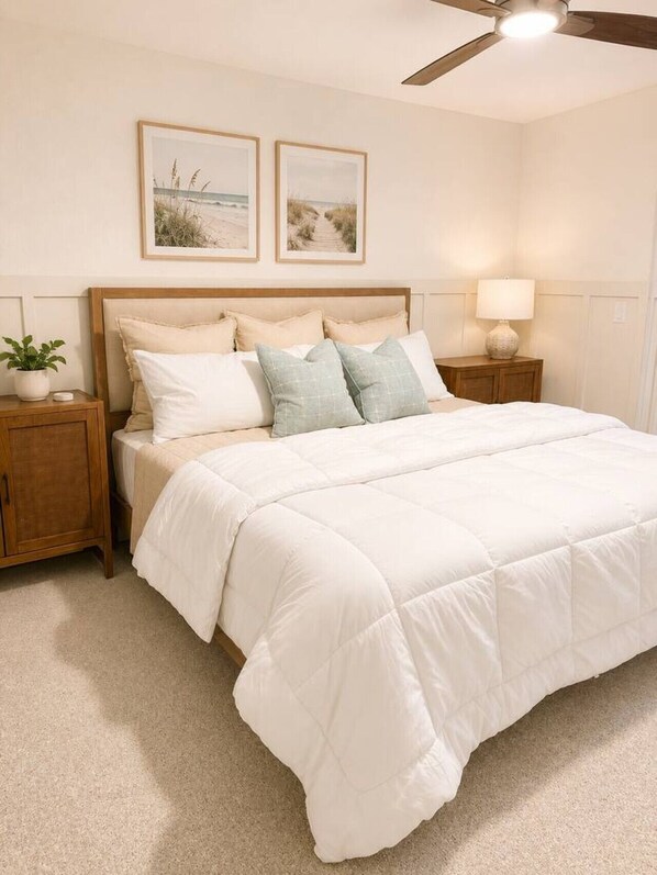 A bedroom with a bed, nightstands, a ceiling fan, and wall art.