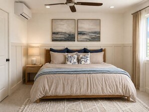 Un dormitorio con cama, mesita de noche, ventilador de techo y dos cuadros colgados en la pared.