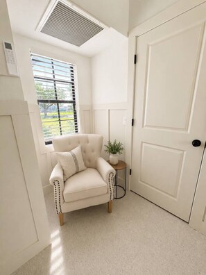 A room with a white door, a window with blinds, a beige armchair, and a small table with a plant. - Luxury Gulf Access Retreat | Gym | Crystal River (Crystal River)