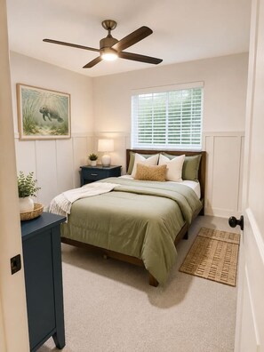 A bedroom with a bed, bedside table, lamp, ceiling fan, window with blinds, and a framed picture on the wall. - Luxury Gulf Access Retreat | Gym | Crystal River (Crystal River)