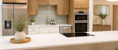 A modern kitchen with wooden cabinets, a stainless steel refrigerator, a double oven, and a large island with bar stools.