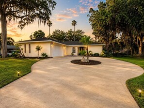 A residential house with a driveway, a garage, and a landscaped front yard with a palm tree. - Luxury Gulf Access Retreat | Gym | Crystal River (Crystal River)