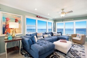 A living room with a large window, a ceiling fan, and a surf-themed decor. - Direct Beachfront | Coastal 3BR Retreat (Bradenton Beach)