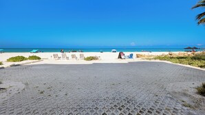 Ein gepflasterter Bereich mit Liegestühlen und Sonnenschirmen, ein klarer, blauer Himmel und das Meer im Hintergrund.