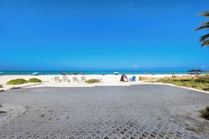 A paved area with beach chairs and umbrellas, a clear blue sky, and the ocean in the background. - Direct Beachfront | Coastal 3BR Retreat (Bradenton Beach)