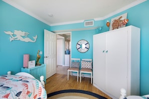 A room with teal walls, a white door, a white wardrobe, a bed with a colorful quilt, a chair with patterned cushions, and a wall clock. - Direct Beachfront | Coastal 3BR Retreat (Bradenton Beach)