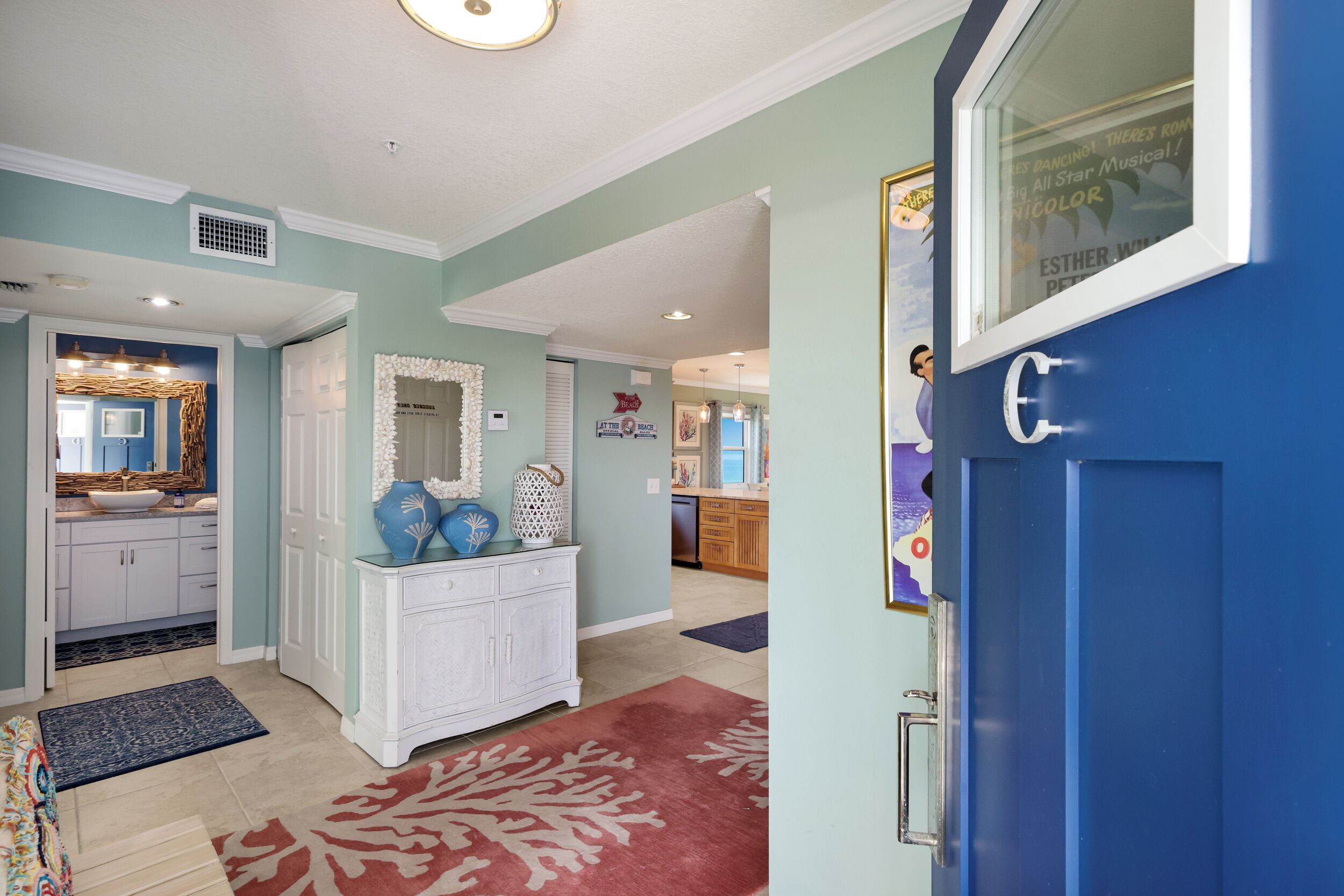 A hallway with a blue door, white cabinetry, a patterned rug, and a kitchen area in the background.