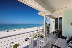 A balcony with a view of a beach and ocean, outdoor seating, and a staircase. - Direct Beachfront | Coastal 3BR Retreat (Bradenton Beach)