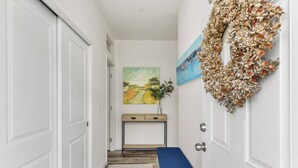 Um corredor com portas brancas, carpete azul, mesa consola de madeira com uma planta e um quadro na parede.