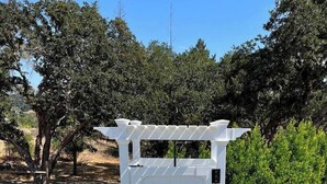 Um portão branco com design simples, inserido em uma área ajardinada com árvores e gramado.