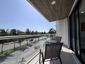 A balcony with a glass railing, a table, and two chairs. - Delightful 2 bedroom Condo & Ocean View Rooftop& just across the beach (Cancún)