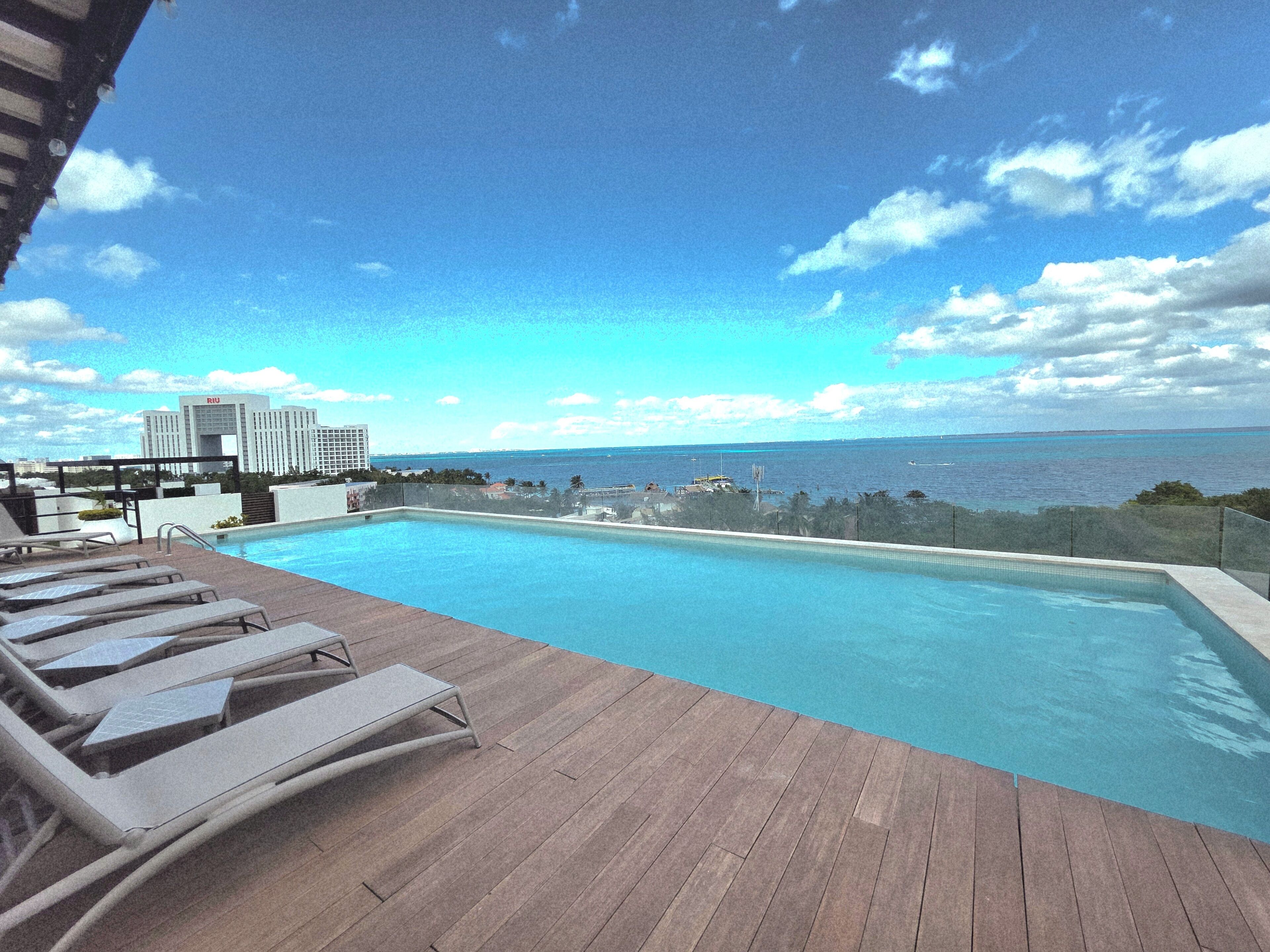 A swimming pool with lounge chairs and a view of the ocean and a distant building.