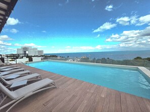 Ein Swimmingpool mit Liegestühlen und Blick auf den Ozean sowie ein Gebäude in der Ferne.