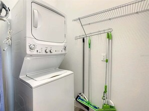 Un espace dédié à la lessive, comprenant un lave-linge, un étendoir et un outil de nettoyage des sols.