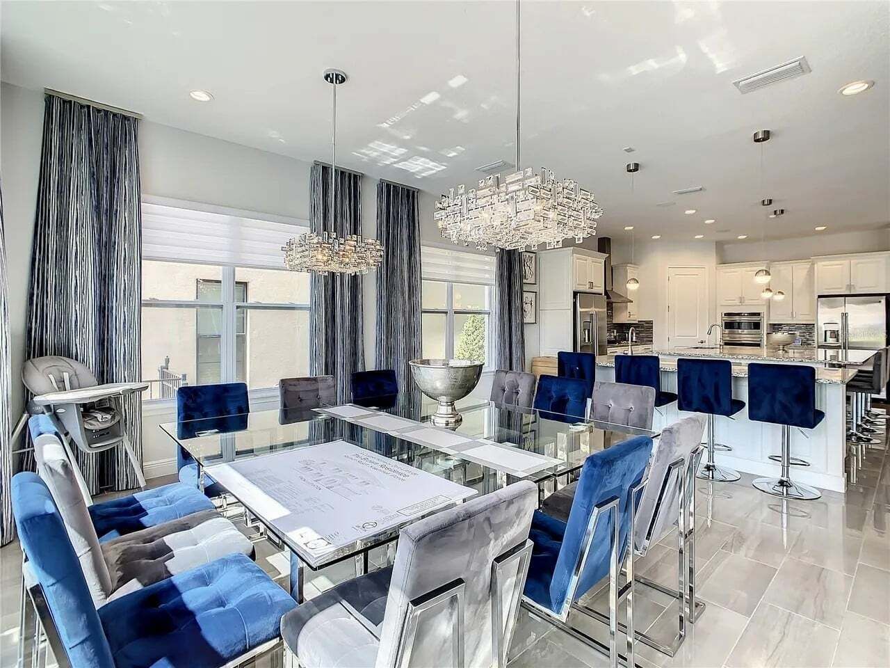 A modern dining area with a glass table, blue upholstered chairs, and a chandelier.