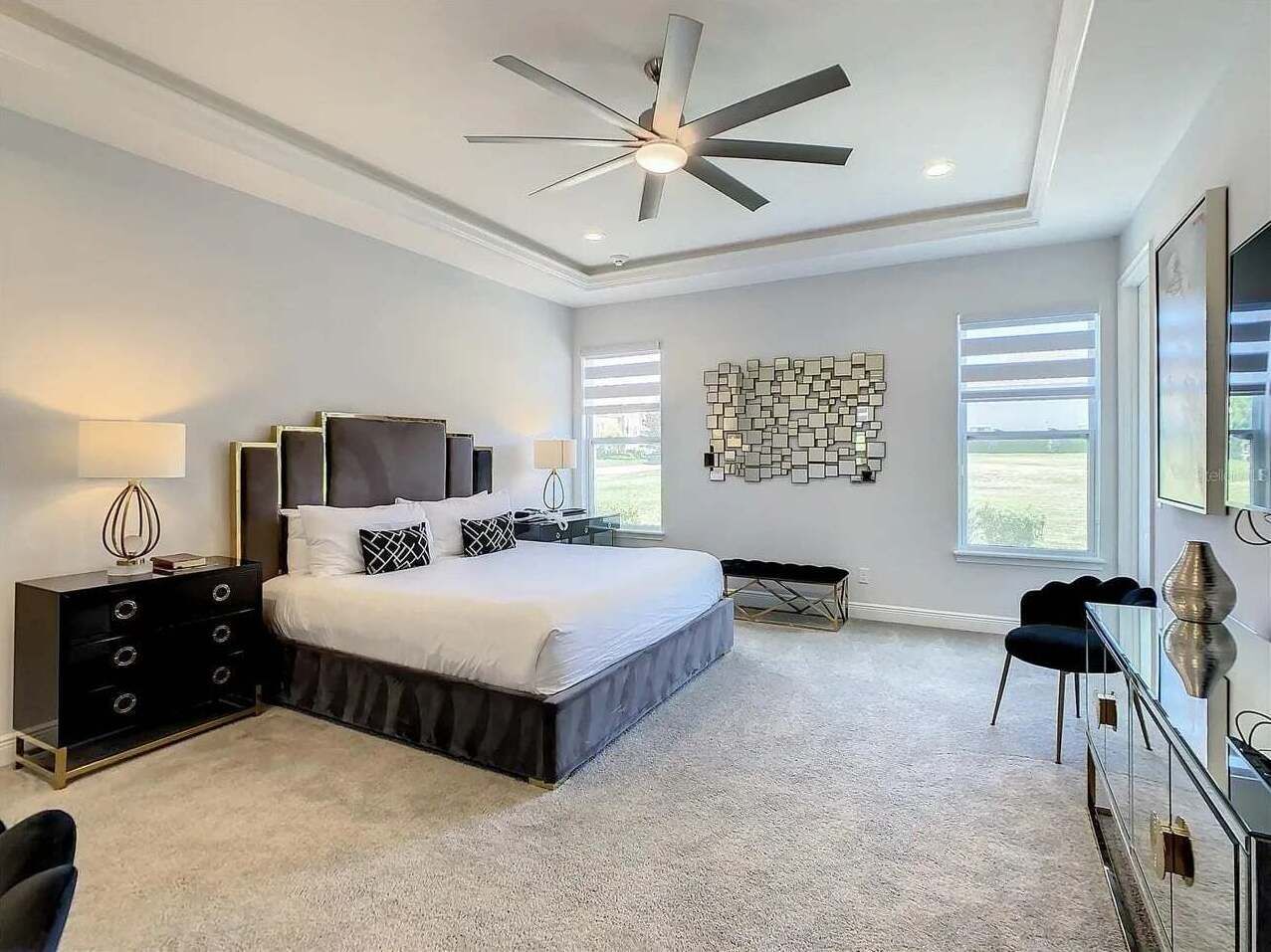 A bedroom with a bed, a dresser, a chair, a ceiling fan, and a window.