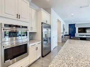 A modern kitchen with stainless steel appliances, white cabinetry, and a granite countertop. - The Reserve at Reunion-TT492 (Kissimmee)
