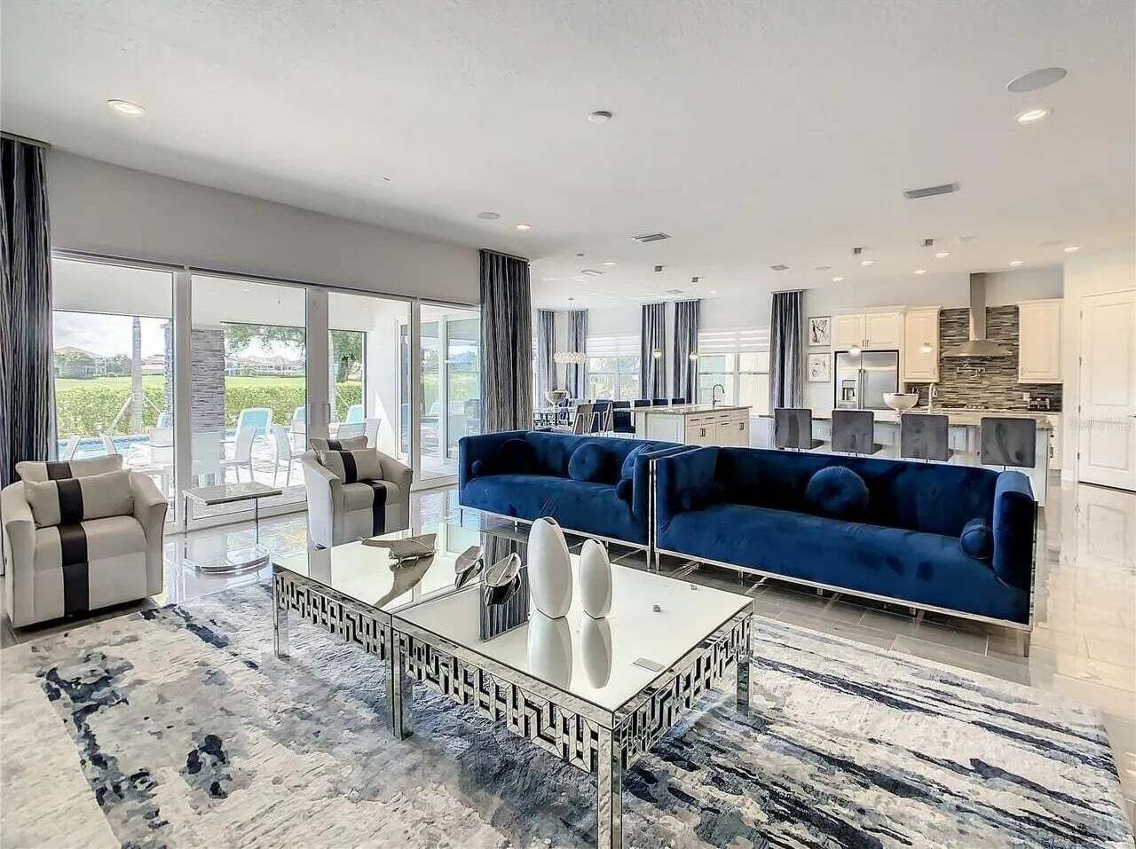 A modern living room with a blue sofa, white armchairs, and a glass coffee table.