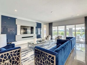 A modern living room with a large flat-screen TV, blue sofas, and a glass coffee table. - The Reserve at Reunion-TT492 (Kissimmee)