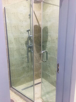 Cabina de ducha con paredes de vidrio, cabezal de ducha de mano y grifo instalado en la pared.