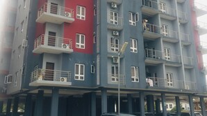Um edifício residencial com vários andares, varandas, área de estacionamento e vista para a rua.