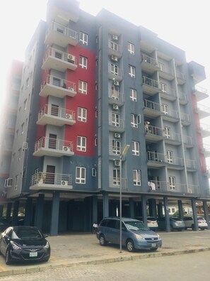 Un edificio residencial de varios pisos con balcones, un estacionamiento y vista a la calle.