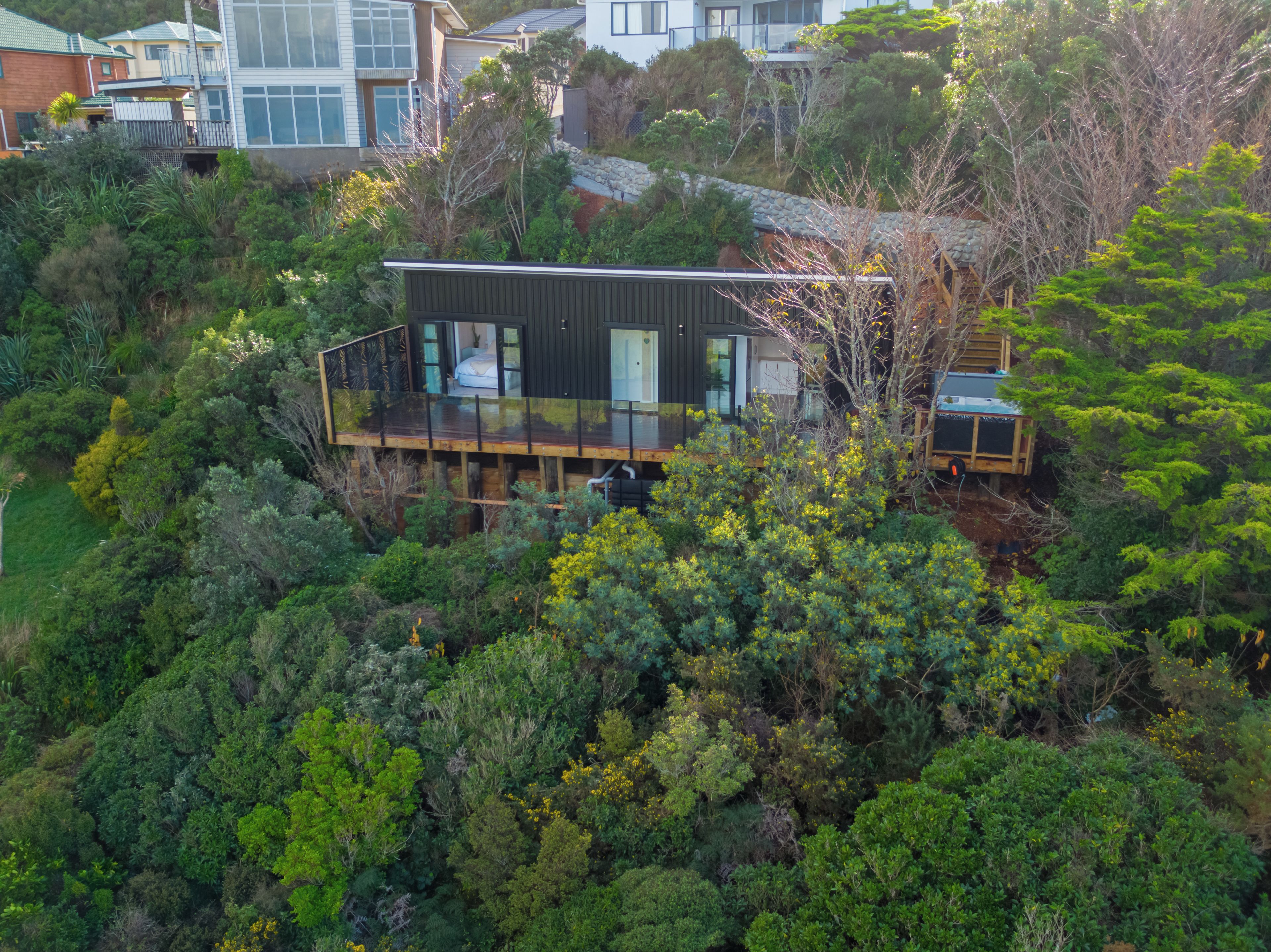 A modern house with a deck, surrounded by dense greenery.