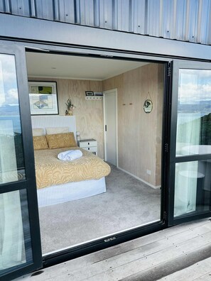 A bedroom with a bed, bedside table, and a view through a glass door. - Pukehuia Paradise – Private Spa Retreat with Wellington Harbour Views (Wellington)