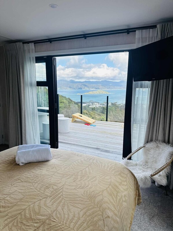 A hotel room with a bed, a view of the sea, and a deck with a shuffleboard.