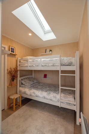 A bunk bed room with a skylight, a small stool, and a shelf with a plant.