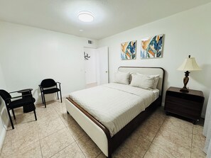 Une chambre à coucher comprenant un lit, un bureau, deux chaises, une table de chevet et deux tableaux accrochés au mur.