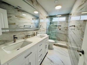 A modern bathroom with marble walls, a glass shower enclosure, and a dual sink vanity. - Cozy 2-bedroom unit in central Westminster, Orange County. (Westminster)